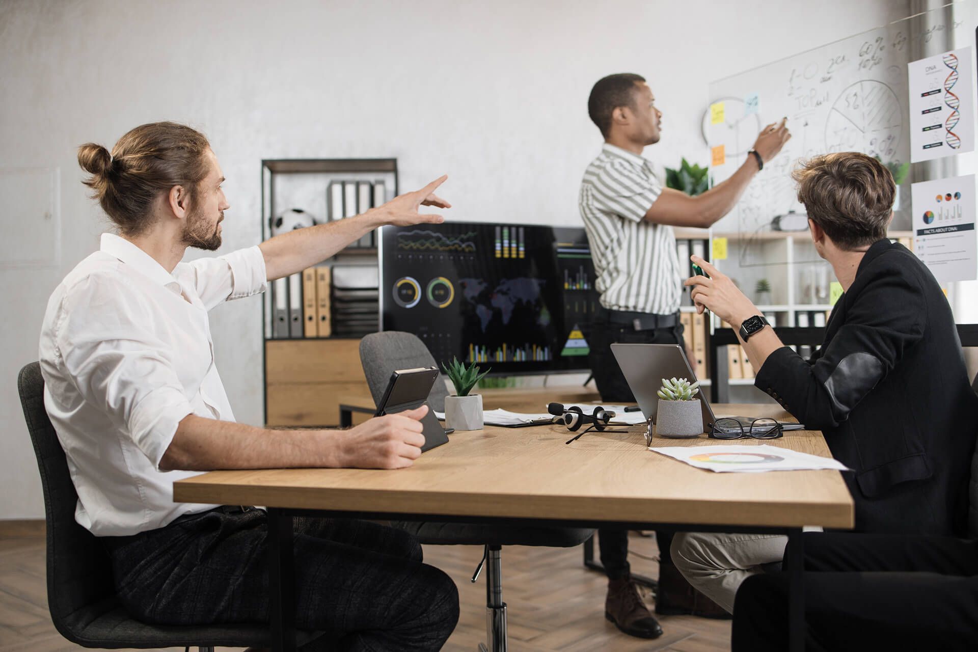 Riunione di lavoro in ufficio: tre persone discutono davanti a un monitor con i grafici delle vendite